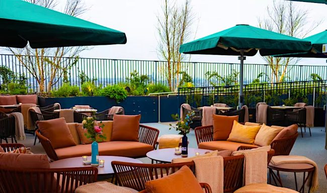 Outdoor lounge area with green umbrellas and orange cushions among lush plants.