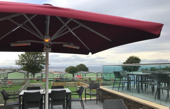 Outdoor dining area with a maroon umbrella, overlooking a scenic landscape.