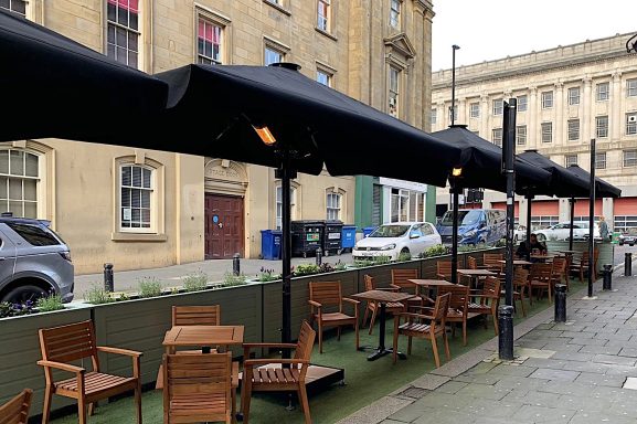Outdoor seating area with wooden tables and chairs under black parasols.