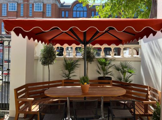 A shaded wooden seating area with a potted plant and greenery backdrop.